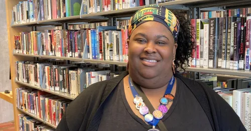 Associate Librarian Kesha Nash poses beside the stacks at Minneapolis Central Library in a bright, patterned headband.